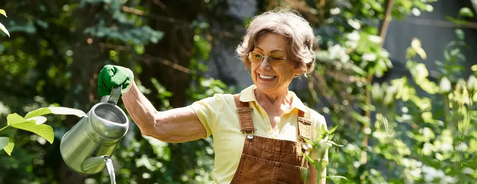 A smiling older woman watering plants in her garden on a sunny day